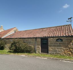 A stone cottage with a tiled roof bushes and a horse weather vane at Beaconsfield Cottage in Burniston near Scalby