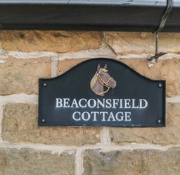 A black sign with a horse head illustration and the text Beaconsfield Cottage on a stone wall at Beaconsfield Cottage in Burniston near Scalby