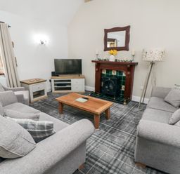 A living room with two grey sofas a tv on a stand a wooden coffee table a fireplace with a mirror above and a lamp at Beaconsfield Cottage in Burniston near Scalby