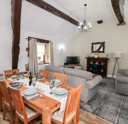 A dining table set for six with a bottle of wine in a living room with sofas a TV and fireplace at Beaconsfield Cottage in Burniston near Scalby