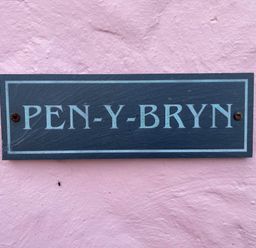 A black and white house name sign reading PEN-Y-BRYN on a pink textured wall at Pen- y- Bryn @ Canllefaes in Penparc near Cardigan