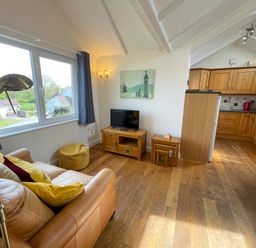 A living room with a sofa and television next to a kitchen with wooden cabinets at Pen- y- Bryn @ Canllefaes Penparc near Cardigan
