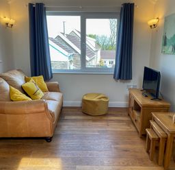 A living room with a leather sofa with yellow cushions a TV on a wooden stand and nested wooden tables at Pen- y- Bryn @ Canllefaes in Penparc near Cardigan