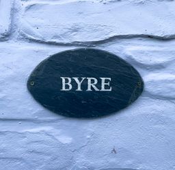 A black oval sign with the word BYRE on a white textured wall at The Byre @ Canllefaes Penparc near Cardigan