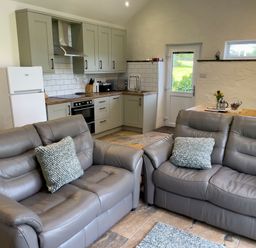 A kitchen and living area with two gray leather sofas and kitchen cabinets at The Byre @ Canllefaes in Penparc near Cardigan