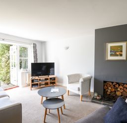 A living room with a sofa armchair round nesting tables TV and a fireplace stocked with firewood at 12 The Gardens in Rousdon