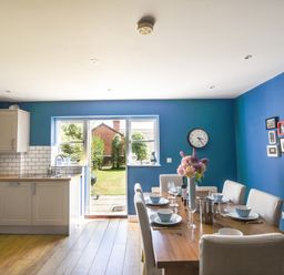 A kitchen and dining area with blue walls a wooden table set with dishes and a vase of flowers at 12 The Gardens in Rousdon
