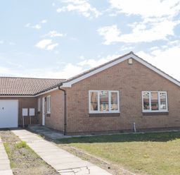 A single-story brick house with a tiled roof two windows a garage and a driveway at 20 Southmead in Amble