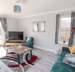 A sitting room with a sofa, armchair, coffee table, television, and windows at 20 Southmead in Amble
