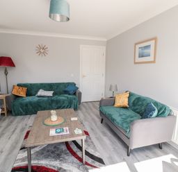 A living room with two sofas a wooden coffee table a floor lamp and a wall clock at 20 Southmead in Amble