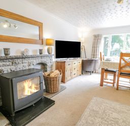 A living room with a fireplace wood burner dining table and chairs a television and a wooden sideboard at Bwthyn Pengwern in Saron near Caernarfon