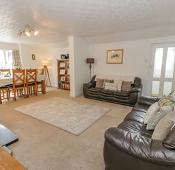 A living room with leather sofas a dining table with chairs a carpet and a bookshelf at Bwthyn Pengwern in Saron near Caernarfon