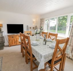 A dining room with a table set for six near large windows with curtains at Bwthyn Pengwern in Saron near Caernarfon