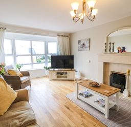 A living room with a sofa, armchair, coffee table, television, fireplace, and large window at 12 Hillview Ludden near Buncrana