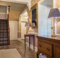 A hallway with wooden furniture table lamps a carpeted staircase and floral wallpaper at Swinside Lodge in Newlands Valley near Keswick