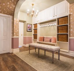 An entryway with white built-in shelves and hooks a cushioned bench wicker baskets pink pillows and a chandelier at Swinside Lodge in Newlands Valley near Keswick