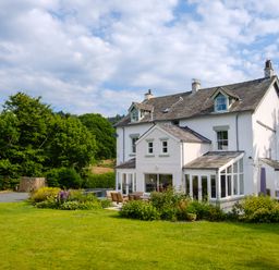 A large white house with an outdoor seating area surrounded by a garden and trees at Swinside Lodge in Newlands Valley near Keswick