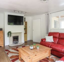 A living room with a red sofa wooden coffee table fireplace and a wall-mounted TV at Haddef Penmaenmawr in Penmaenmawr