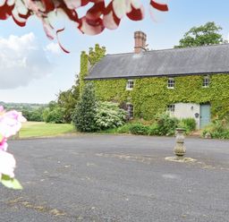 A courtyard with a stone pedestal in front of a building covered with ivy at Scarvagh House in Scarva near Loughbrickland
