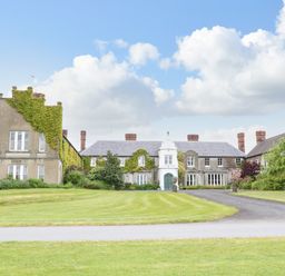 A large historic house with ivy on walls surrounded by green lawn and a driveway at Scarvagh House in Scarva near Loughbrickland