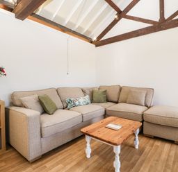 A living room with a beige sectional sofa a wooden coffee table and flowers on a side table at The Old Kennels in Harcombe near Sidford
