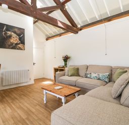 A living room with a beige sofa a wooden coffee table flowers on a side table and a dining table with chairs at The Old Kennels in Harcombe near Sidford