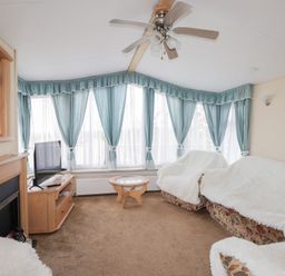 A living room with a ceiling fan a television on a wooden stand a glass coffee table and sofas with white covers at The Cabin in Occumster near Lybster