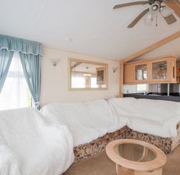 A living room with a sectional sofa covered with white throws a glass coffee table a ceiling fan and blue curtains at The Cabin in Occumster near Lybster