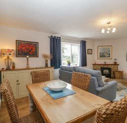 A dining area with a wooden table and woven chairs next to a living room with a gray sofa a fireplace and a wall-mounted TV at Phocle Ridge in Phocle Green near Ross-On-Wye