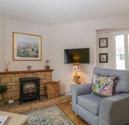 A living room with a grey armchair a fireplace and a wall-mounted television at Phocle Ridge in Phocle Green near Ross-On-Wye