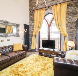 A living room with brown leather sofas yellow cushions a yellow rug and a TV in front of arched windows at The Upper Room in Ballymena