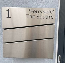 A metal sign on a wall showing number 1 and Ferryside The Square with two empty panels