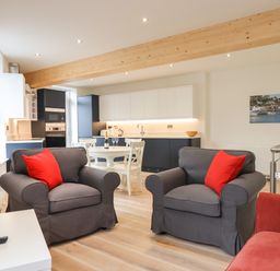 A living room with two gray armchairs with red cushions and an open kitchen with black and white cabinets at Ferryside in Kingswear