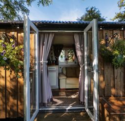 An open wooden cabin door with curtains leading to a room with a sofa and kitchenette at The Shepherd's Rest in Robin Hood's Bay