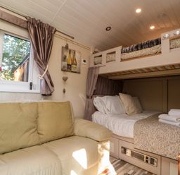 A room with a cream leather sofa with cushions a bunk bed with folded towels and bedding and a window with curtains at The Shepherd's Rest in Robin Hood's Bay