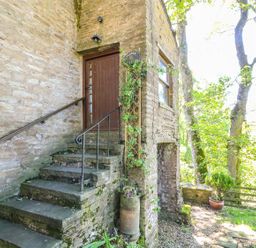 Stone steps with metal railings leading to a wooden door on a stone building surrounded by trees and plants at Keepers in Nenthead near Alston