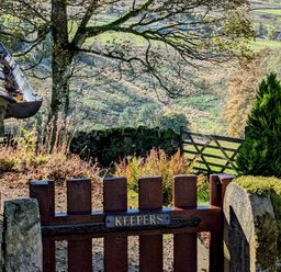 A wooden garden gate with a sign saying Keepers opening to a countryside view with trees and a wooden fence at Keepers in Nenthead near Alston