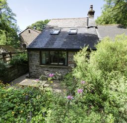 A stone cottage with a slate roof surrounded by green plants and flowers at Bothy in Nenthall near Alston