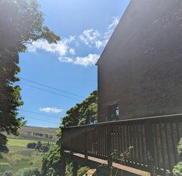 An outdoor view of a balcony attached to a stone building with trees and a grassy hill in the background at Chestnut in Nenthall near Alston