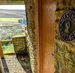 A wooden door with a sign that reads Chestnut Cottage on a stone wall with a countryside view in the background at Chestnut in Nenthall near Alston