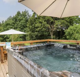 An outdoor hot tub on a wooden deck with umbrellas and trees in the background at Penarth in Cregrina near Builth Wells