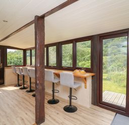 A sunroom with bar stools along a wooden counter by windows and a wooden door at Penarth in Cregrina near Builth Wells