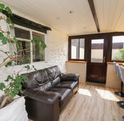 A room with a black leather sofa a potted plant windows and a high wooden table with gray stools at Penarth in Cregrina near Builth Wells