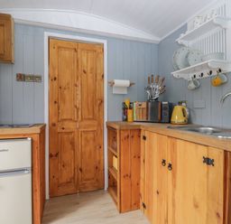 A kitchen with wooden cabinets a fridge a sink a microwave and plates on a wall shelf at Rabbit Hill Hut in Govilon