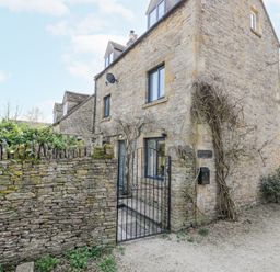 A stone house with a metal gate and a stone wall at The Old School House in Lower Swell near Stow-On-The-Wold