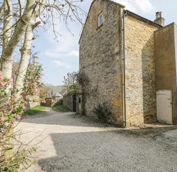 A gravel pathway beside a stone building with a wooden door and flowering trees at The Old School House in Lower Swell near Stow-On-The-Wold