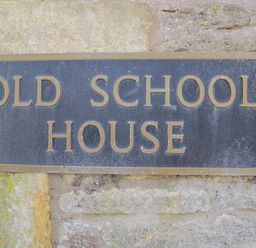 A close up of a black and gold sign on a stone wall that reads Old School House at The Old School House in Lower Swell near Stow-On-The-Wold