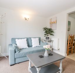 A living room with a blue sofa white pillows coffee table with flowers and a plant at Thornhills Cottage in Othery near Middlezoy