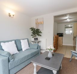 A living room with a blue sofa white pillows coffee table with flowers and a view into a kitchen and dining area at Thornhills Cottage in Othery near Middlezoy