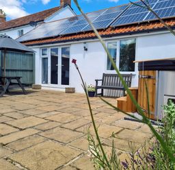 A patio with a wooden bench hot tub picnic table and solar panels on the roof at Thornhills Cottage in Othery near Middlezoy